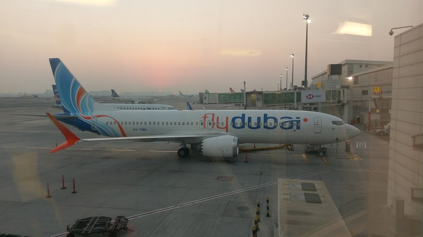 A flydubai Boeing 737 MAX parked at a gate at Dubai International Airport at sunrise