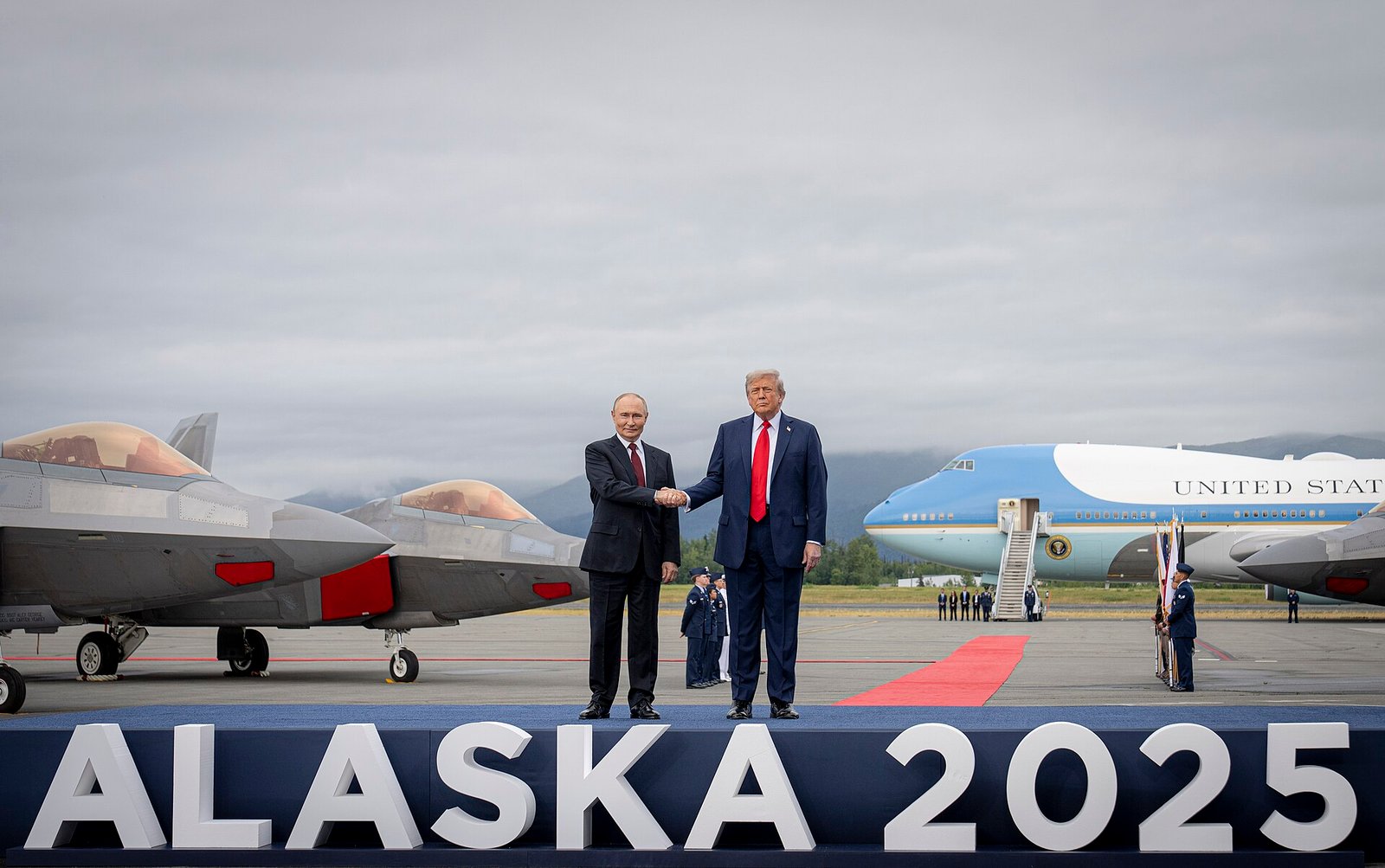 Donald Trump and Vladimir Putin shaking hands on a red carpet at Joint Base Elmendorf-Richardson in Alaska in August 2025