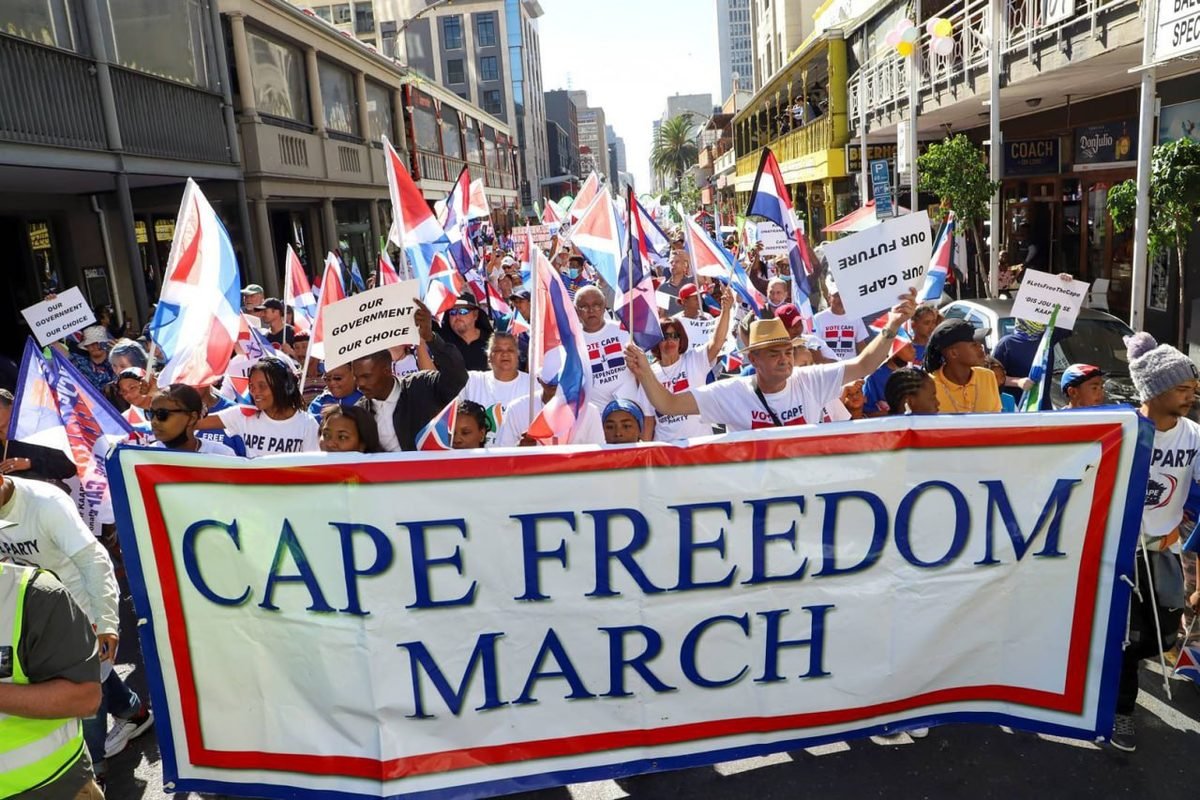 Supporters march behind a Cape Freedom March banner in central Cape Town, waving blue, white and orange-red Cape flags